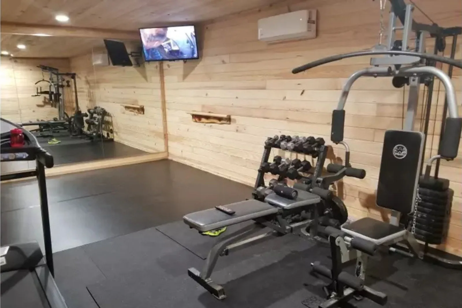 Durable black rubber gym flooring Home gym with light wood paneling and durable black rubber gym flooring, providing a supportive and resilient surface for exercise equipment and weight training.