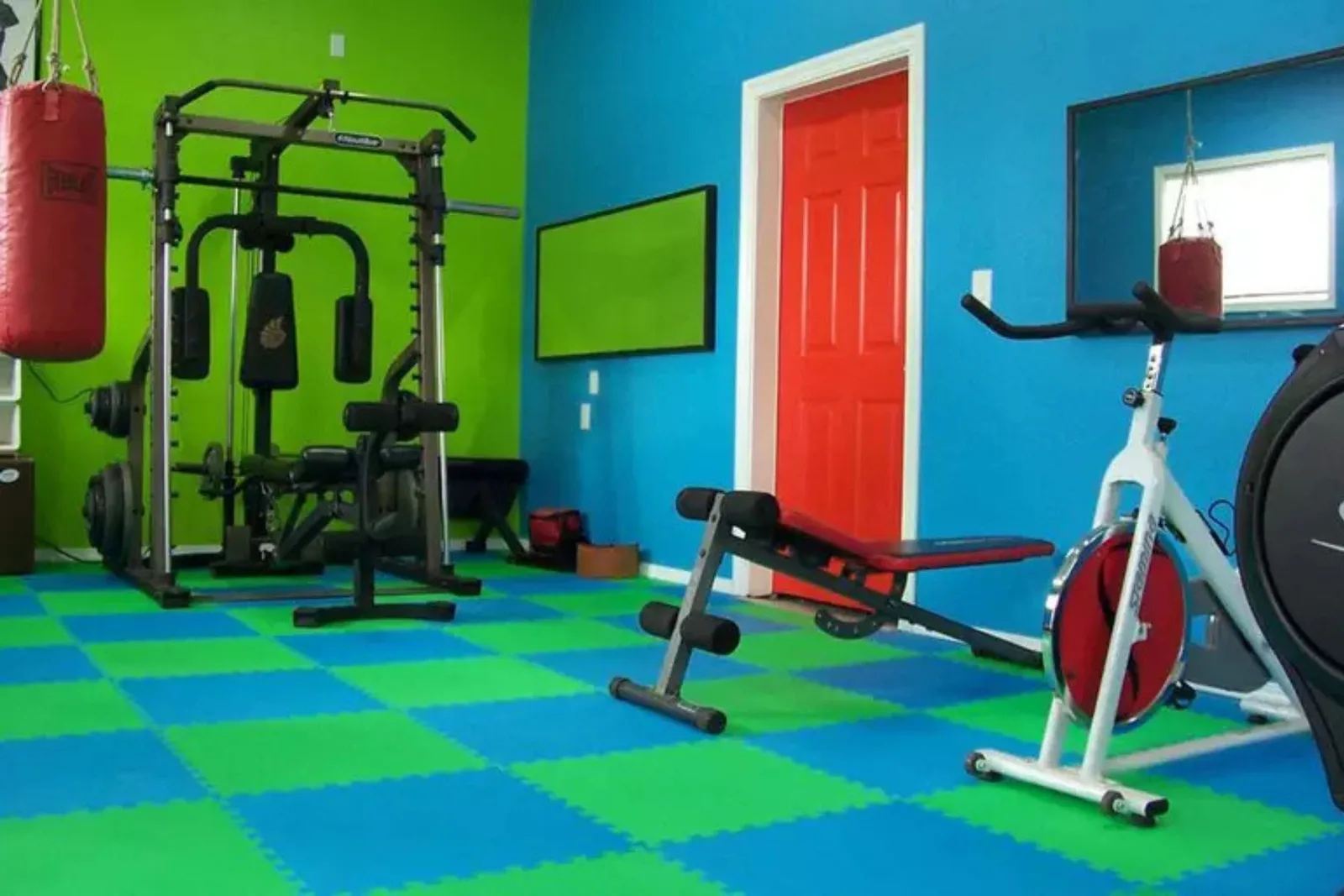 Durable interlocking foam floor tiles Vibrant home gym with durable blue and green interlocking foam floor tiles, providing a colorful and shock-absorbing surface for exercise equipment and weight training.