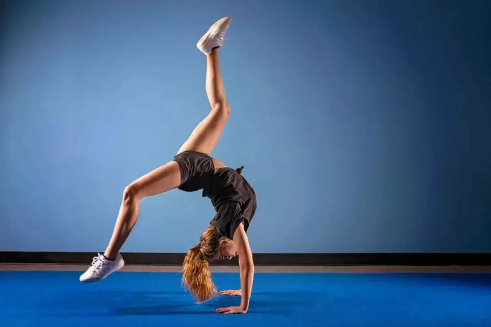 Durable blue rubber gym flooring Gymnast performing a handstand bridge on durable blue rubber flooring against a blue wall, showcasing a supportive surface for acrobatic training.