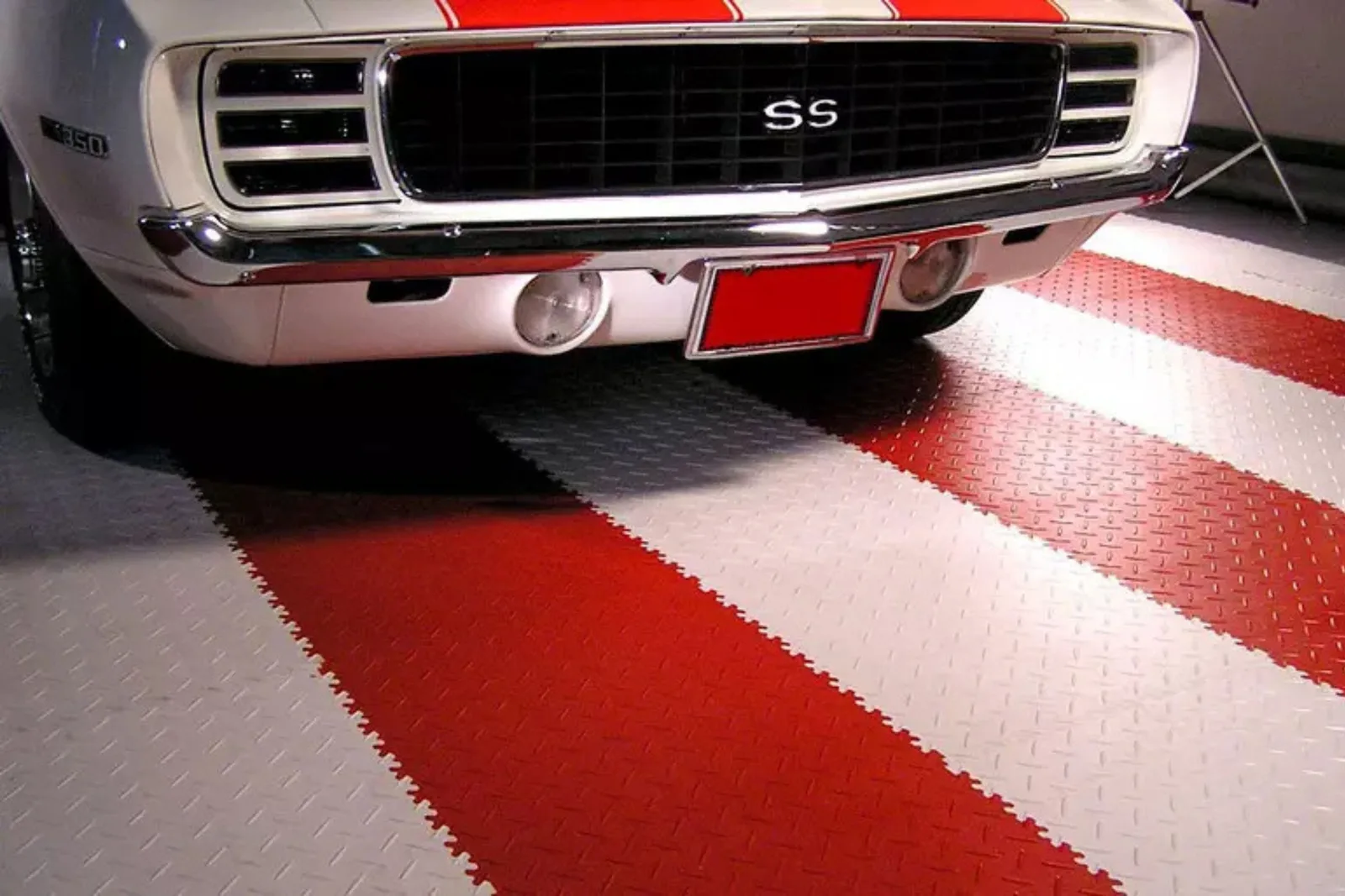 Durable checkered plastic garage tiles Classic white car parked on durable red and white checkered plastic garage tiles with a diamond-plate pattern, creating a high-performance showroom floor.