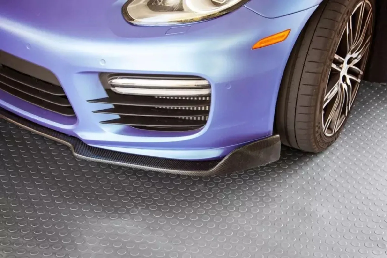Durable gray coin-pattern garage rolls Close-up of a blue sports car parked on durable gray coin-pattern garage flooring rolls, providing a protective and non-slip surface.