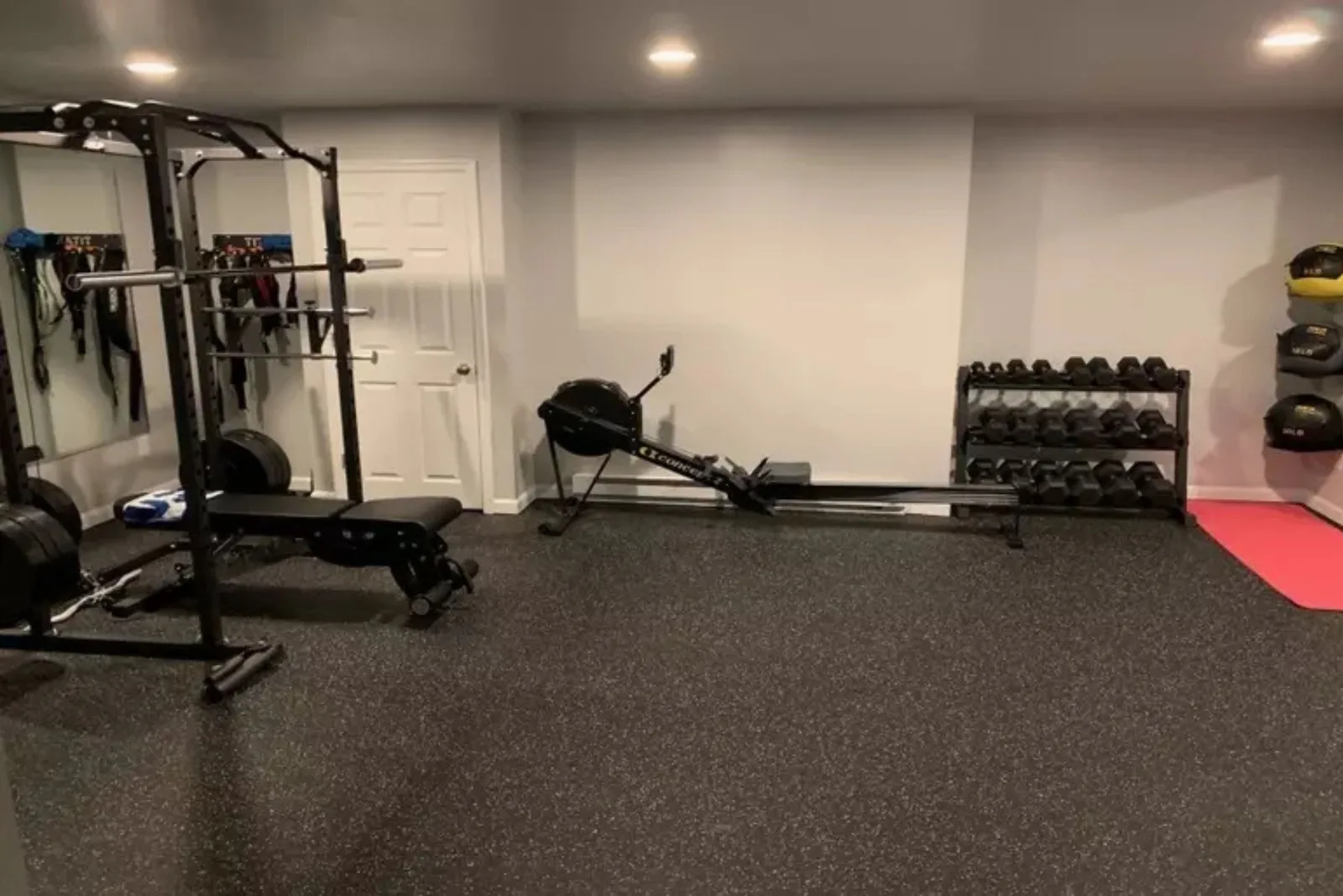 Durable speckled rubber gym flooring Modern home gym featuring a rowing machine, squat rack, and dumbbells on durable black speckled rubber gym flooring, providing a protective and high-performance surface.