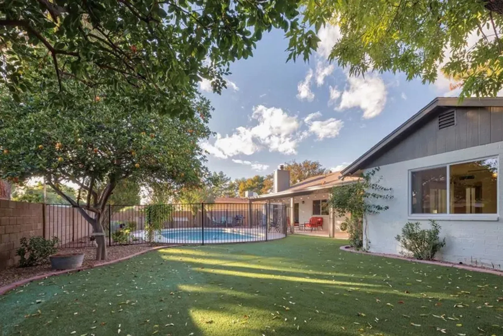 Artificial grass for residential landscaping creates a lush, green, and low-maintenance lawn in a backyard with a swimming pool and patio.