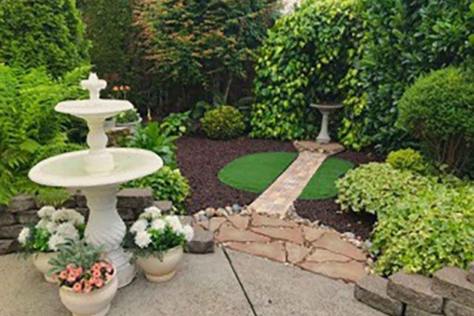 Greenspace artificial grass rug provides a lush, vibrant green, and low-maintenance focal point in a manicured garden with a stone pathway and fountain.