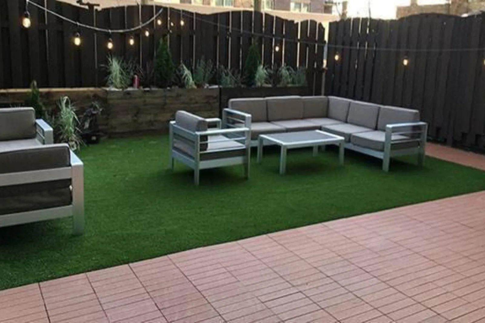 Composite deck tiles and artificial grass create a modern, low-maintenance, and professional outdoor patio with a seating area and landscaping.