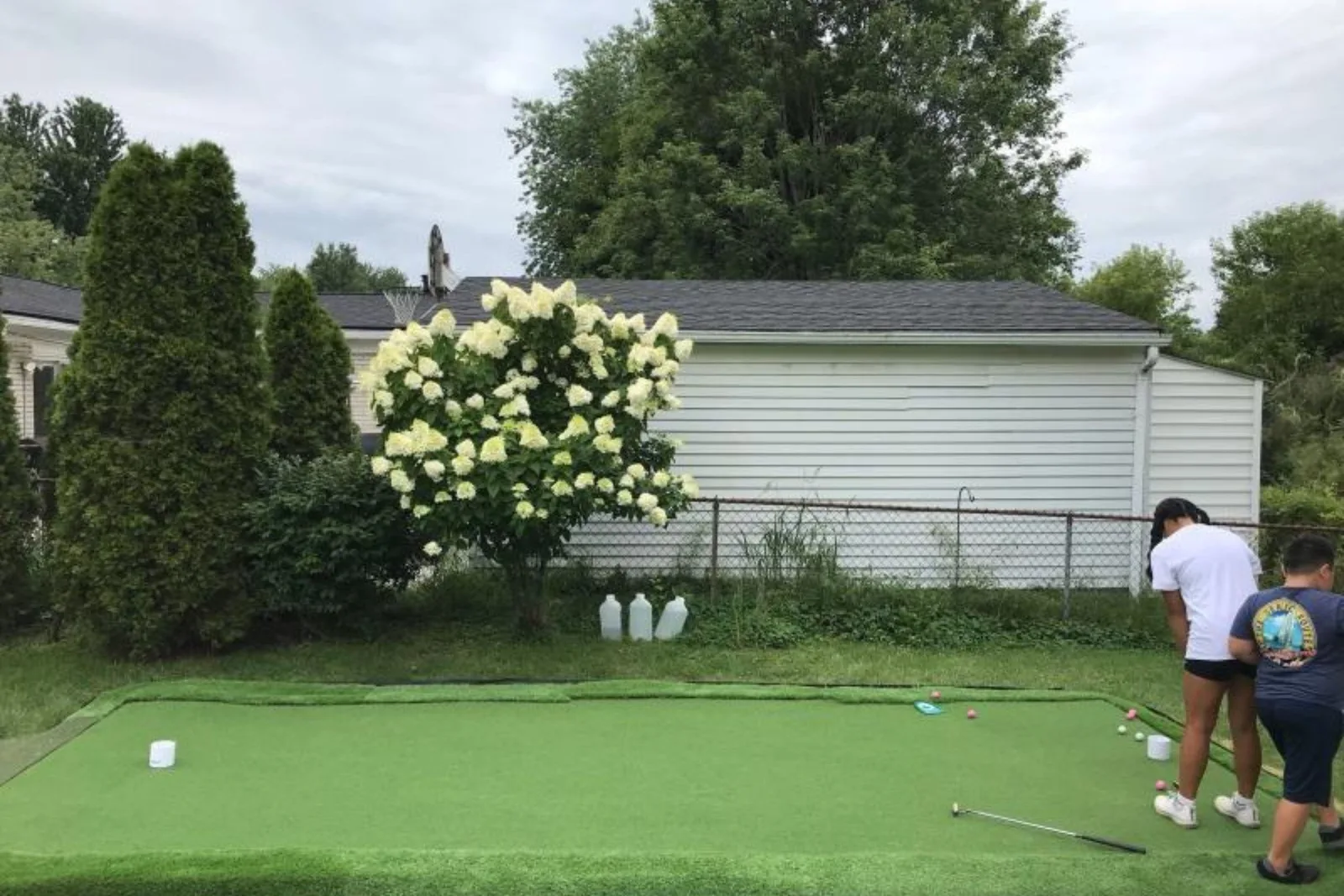 Putting green turf provides a low-maintenance and professional-looking surface for a backyard golf putting green, with a family practicing their putting strokes.