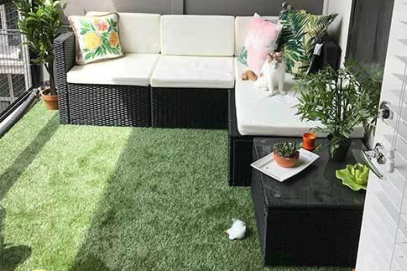 Artificial turf or fake grass provides a lush, low-maintenance, and pet-friendly flooring solution for a small outdoor balcony with a couch and plants
