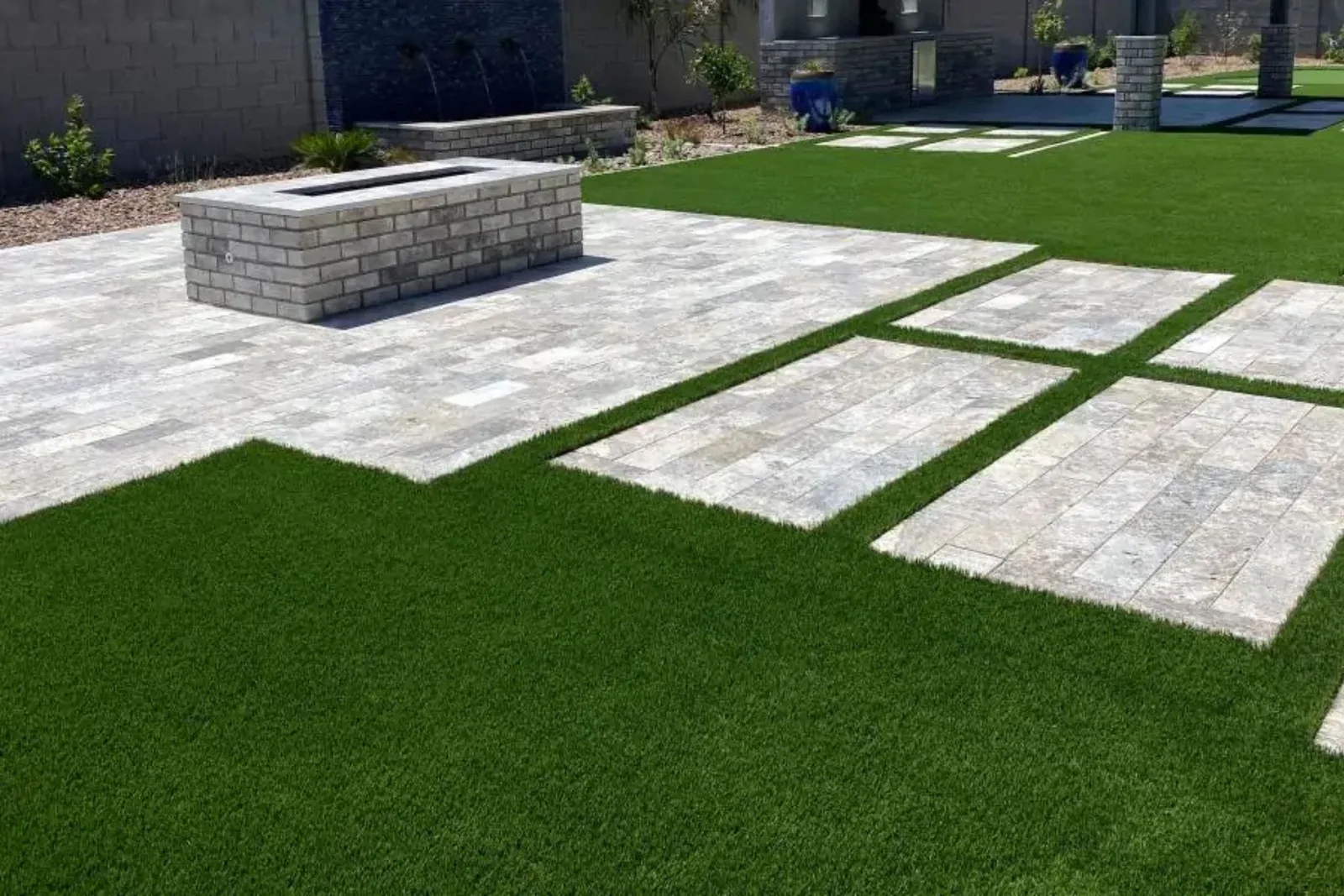 Artificial grass lawn turf creates a modern, low-maintenance, and lush green landscape, accented by stone pavers and a fire pit in a residential backyard.