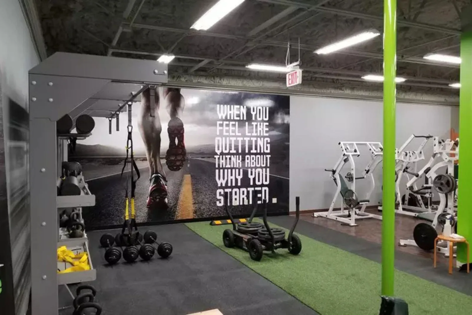 Artificial grass gym turf provides a durable and low-impact flooring solution for a fitness center, with a sled, dumbbells, and other athletic equipment.