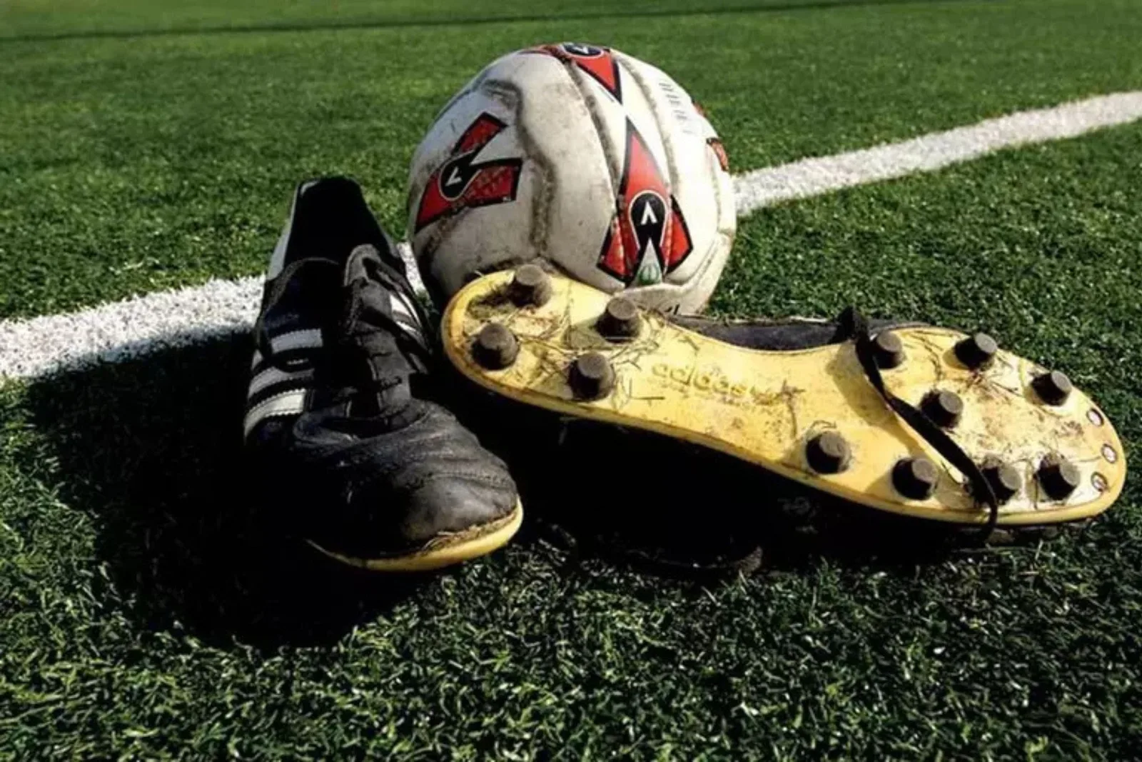 Sports field turf provides a durable and low-maintenance surface for a soccer field, with an old soccer ball and a pair of cleats on the green synthetic grass.
