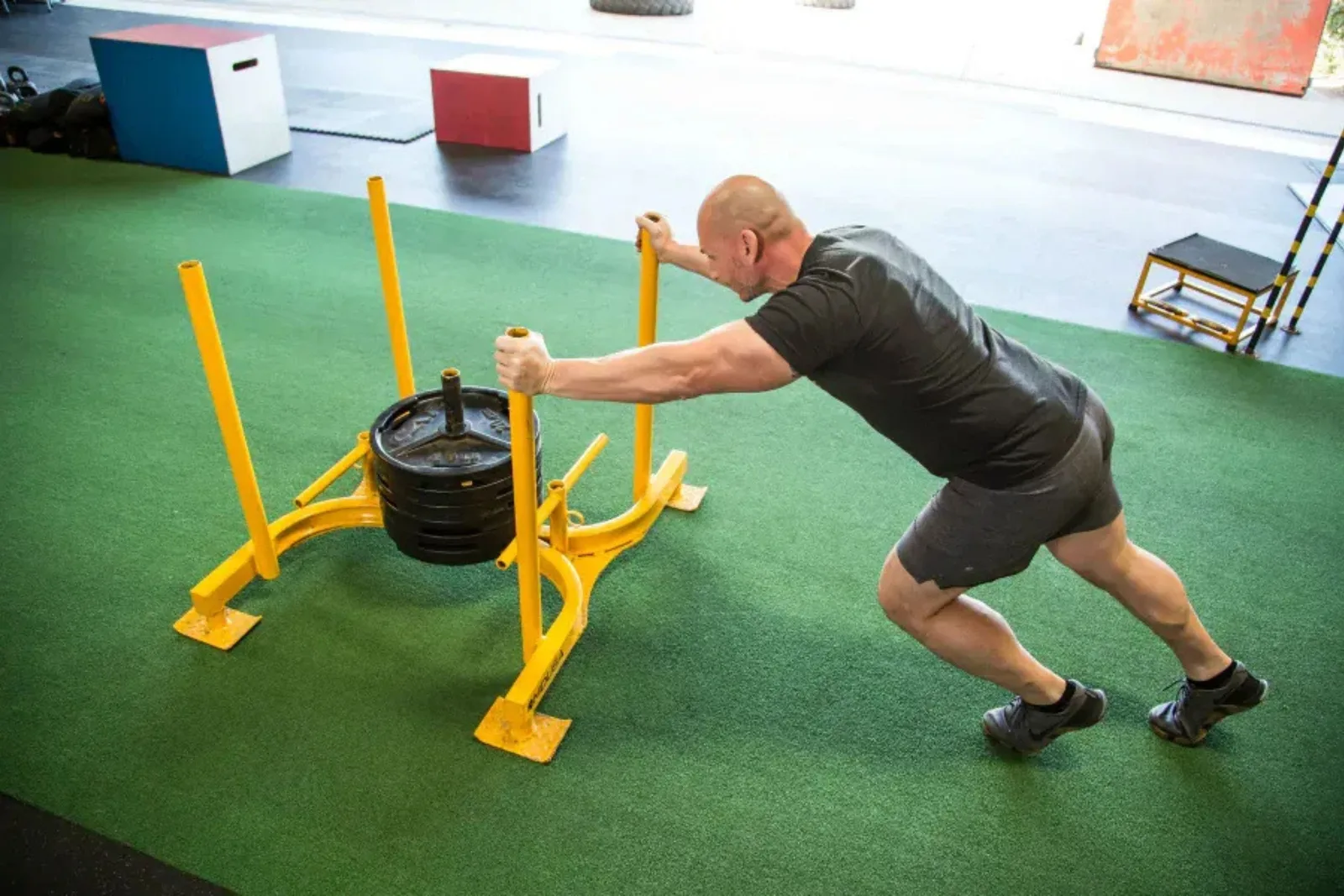 Artificial grass gym turf provides a durable, low-impact, and high-performance flooring solution for athletic training, with a man performing sled pushes on a green field.