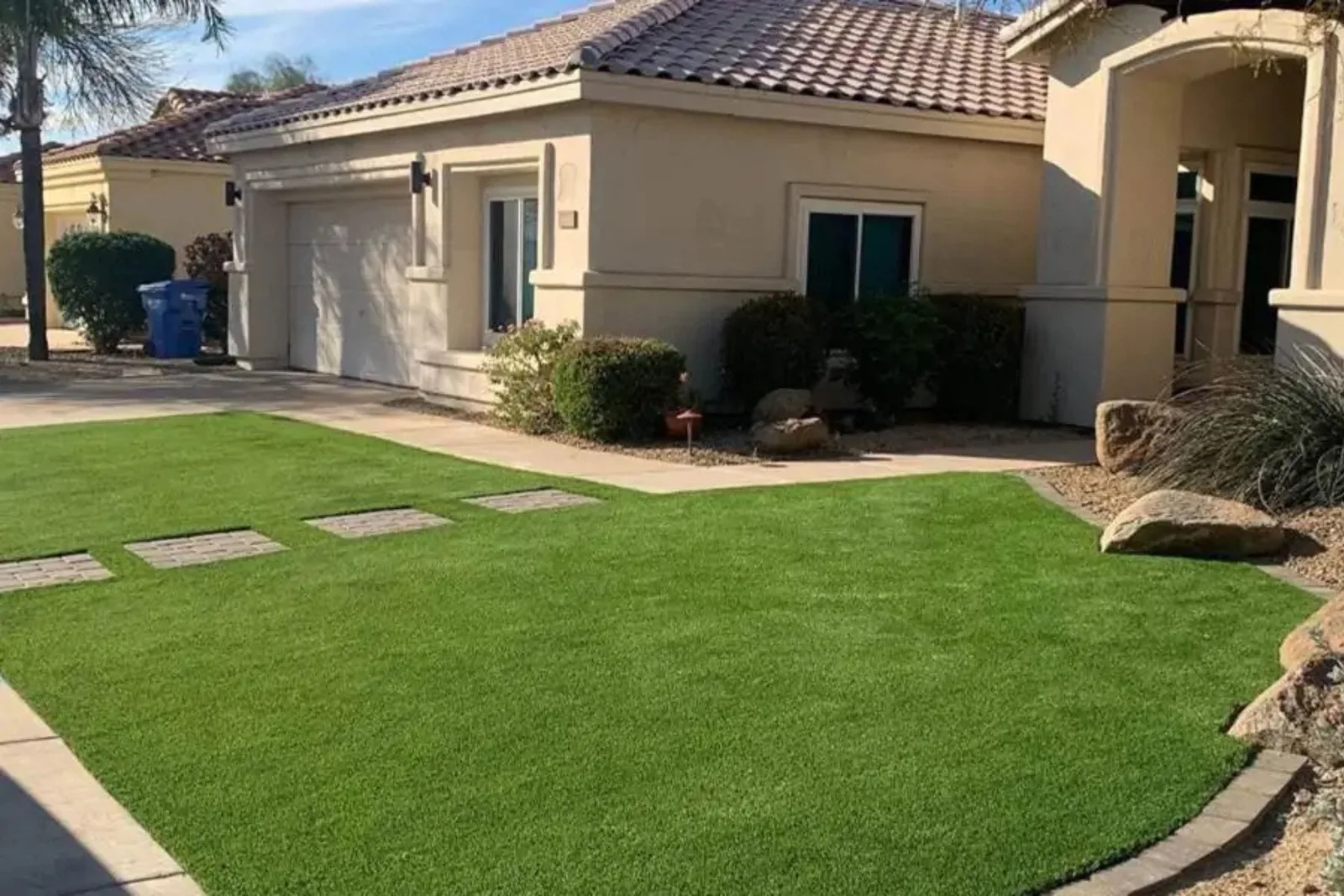 Artificial grass landscaping turf provides a lush, low-maintenance, and drought-friendly lawn in a residential front yard with a walkway and stone accents.
