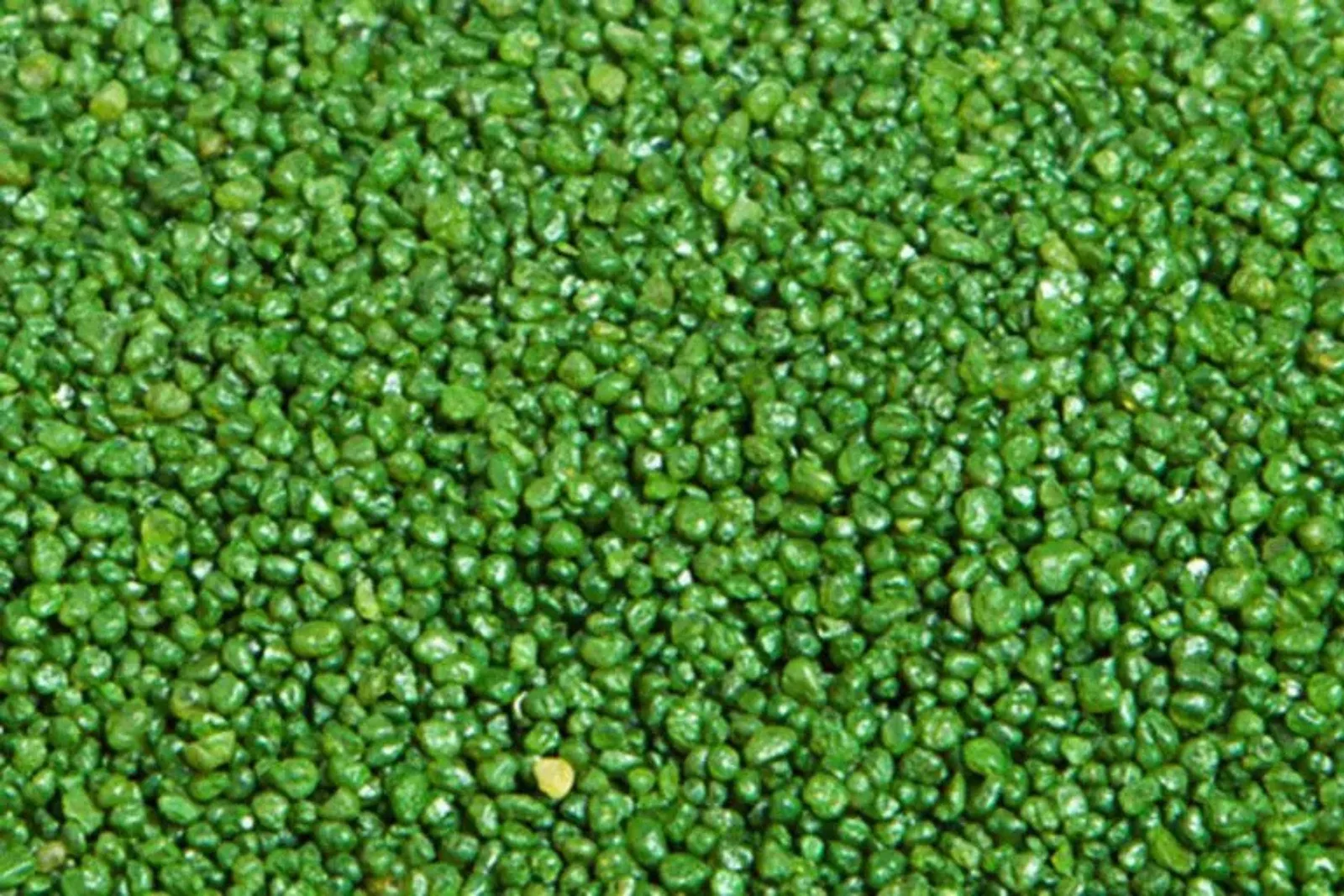 A close-up texture shot of green turf infill, showcasing the small granules used to weigh down and support the blades of artificial grass on sports fields and lawns.