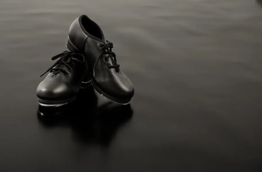 Tap shoes mid-step on a black marley dance floor roll