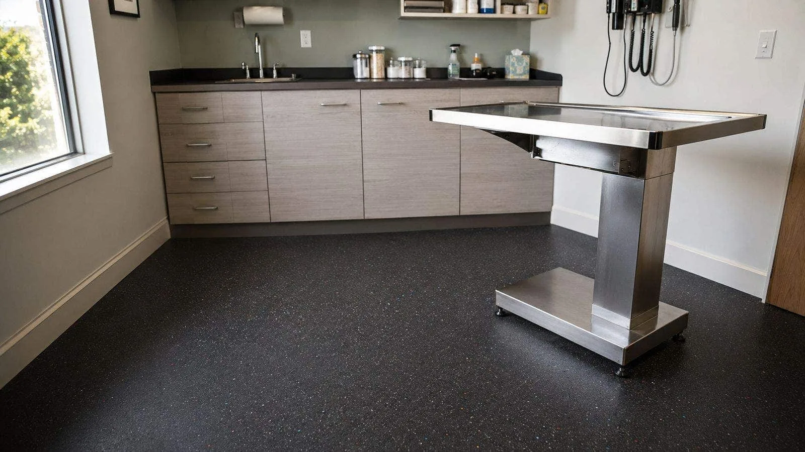 Veterinary clinic treatment area with a dark commercial rubber floor and a stainless steel exam table