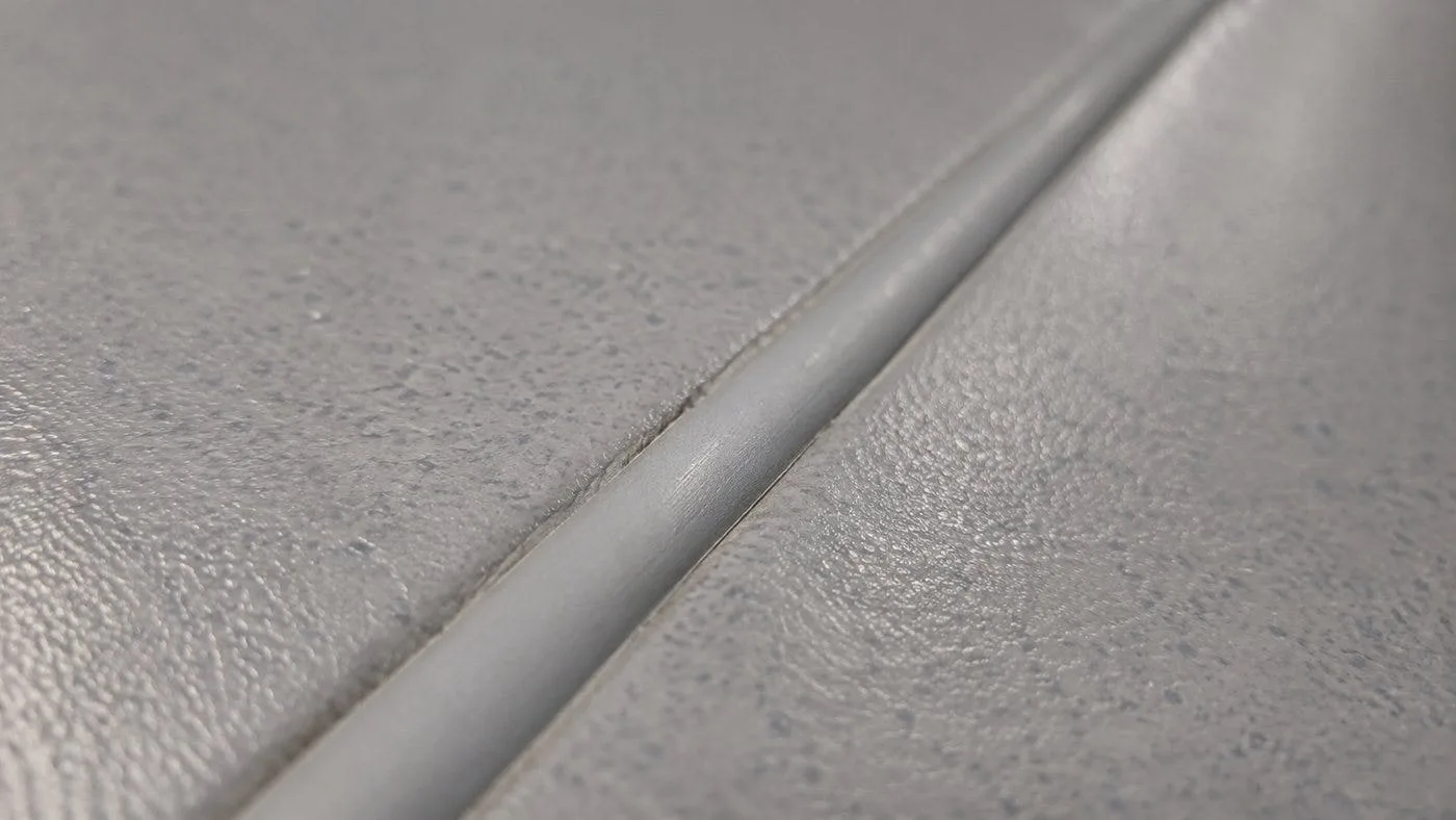 Close-up of a heat-welded PVC seam in commercial sheet vinyl flooring showing the fused weld rod
