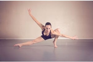 A dancer on marley dance flooring posing in a crouched position