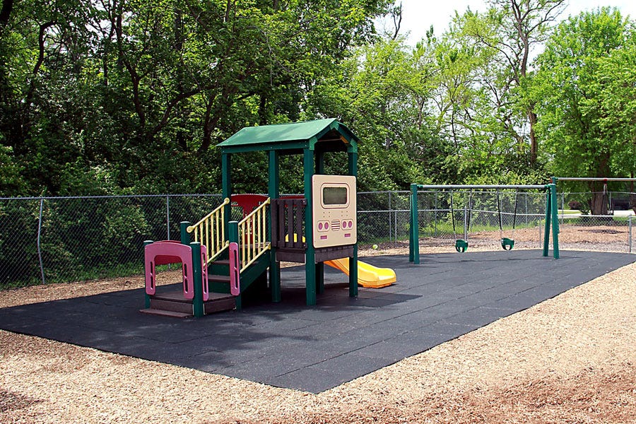 Black playground tiles over wood mulch with a commerical playground