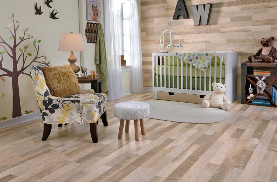 nursery scene of light laminate flooring, a chair, stool, and a crib with toys