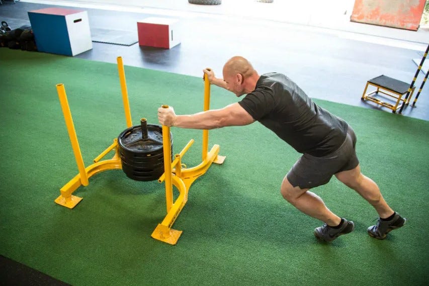A man pushing a weight sled on gym turf