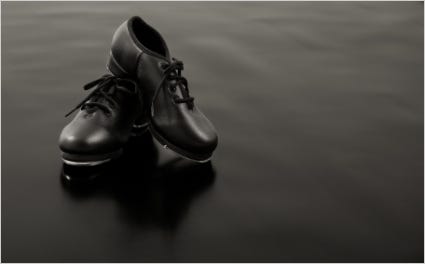 close up of black tap shoes with laces on black marley dance floor